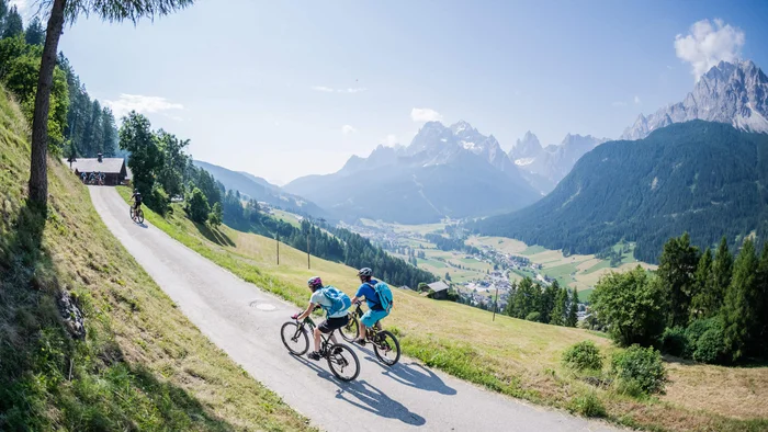 Twee fietsers op bergweg met uitzicht op dal en bergen in zonlicht