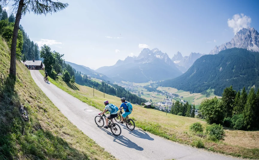 Zwei Radfahrer auf Bergstraße mit Blick auf Tal und Berge im Sonnenschein
