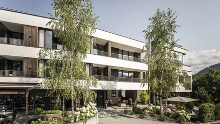 Modernes dreistöckiges Gebäude mit Bäumen und Sitzbereichen im Hof