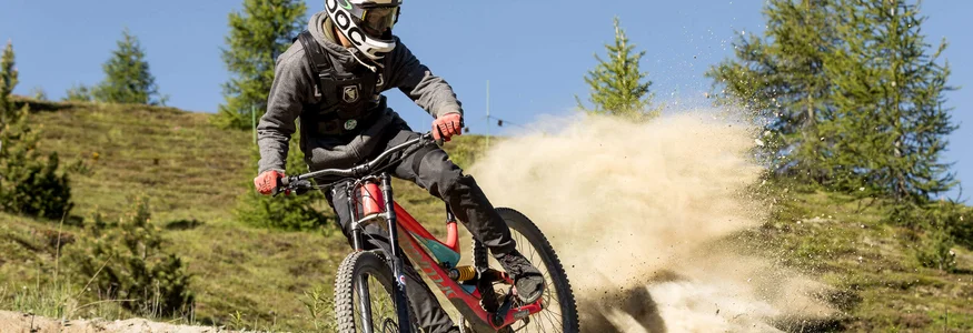 Mountainbiker in voller Montur fährt auf staubigem Weg durch bergige Landschaft