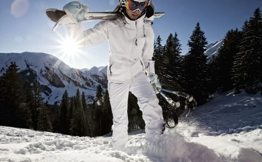 Skifahrerin in weißer Kleidung mit Skiern und Stöcken im Schnee vor Bergen