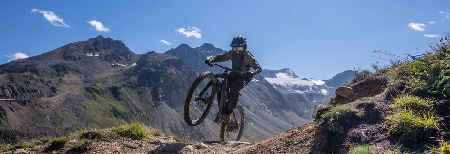 Mountain biker performing a wheelie on a sunny mountain trail