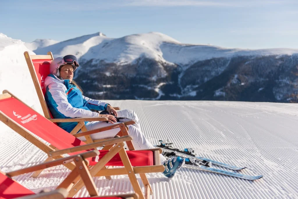 Sonnenskilauf & Therme im März / 5 Nächte Vrouw in skikleding zittend op rode ligstoel in de sneeuw met bergen op de achtergrond