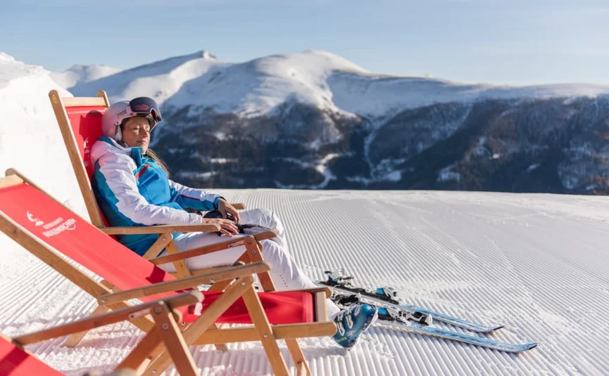 Sonnenskilauf & Therme im März / 5 Nächte Vrouw in skikleding zittend op rode ligstoel in de sneeuw met bergen op de achtergrond
