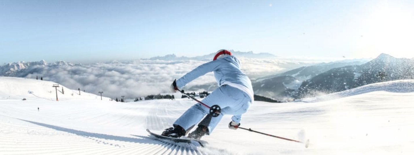 Skifahrer in weißer Kleidung fährt auf präparierter Skipiste bei klarem Himmel