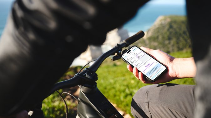 Person hält Smartphone mit Fahrrad-App neben Fahrradlenker im Freien