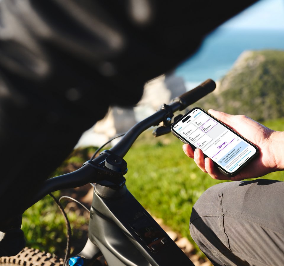 Das Abenteuer ruft und dein eBike hört zu! © Bosch eBike Systeme Person hält Smartphone mit Fahrrad-App neben Fahrradlenker im Freien
