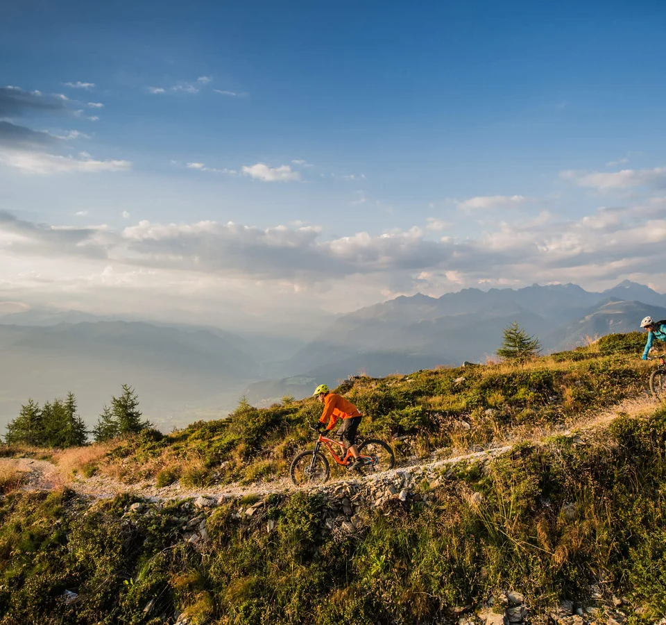 Zwei Mountainbiker fahren auf einem Bergweg bei Sonnenuntergang