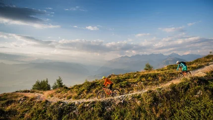 Zwei Mountainbiker fahren auf einem Bergweg bei Sonnenuntergang