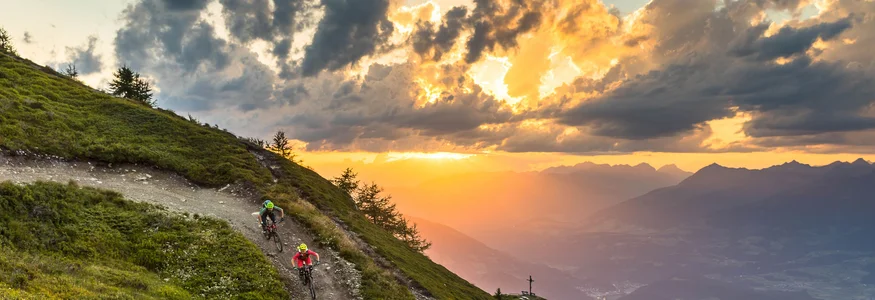 Zwei Mountainbiker fahren auf Bergpfad bei Sonnenuntergang