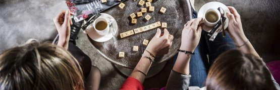 Adam & Adam meet eva, Zwei Personen spielen Buchstabenspiel am Tisch mit Kaffee und Magazin