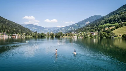 Mensen op paddleboards op een meer met bergen en dorpen op de achtergrond