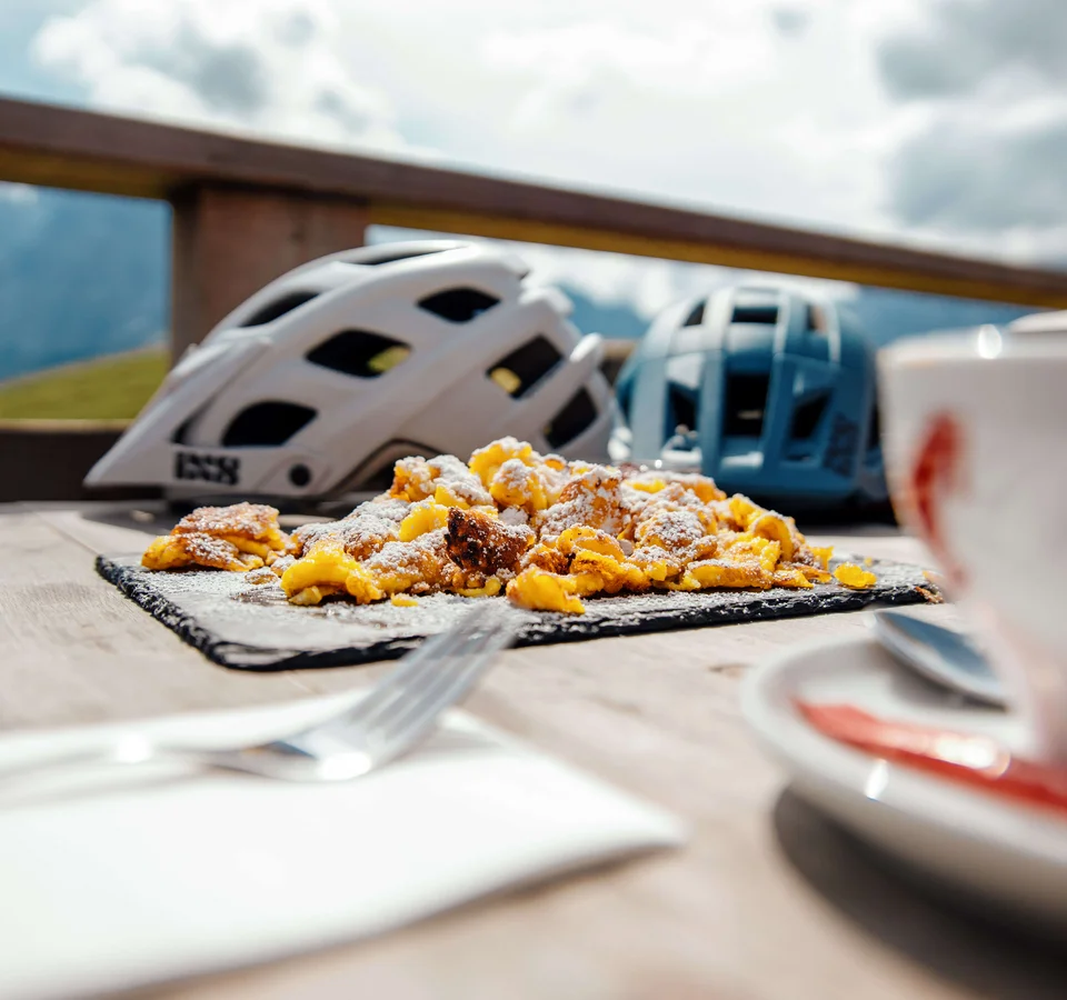 Bergfrühstück mit Kaiserschmarrn und Fahrradhelmen auf Holztisch