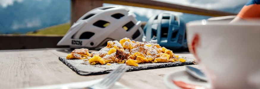 Bergfrühstück mit Kaiserschmarrn und Fahrradhelmen auf Holztisch