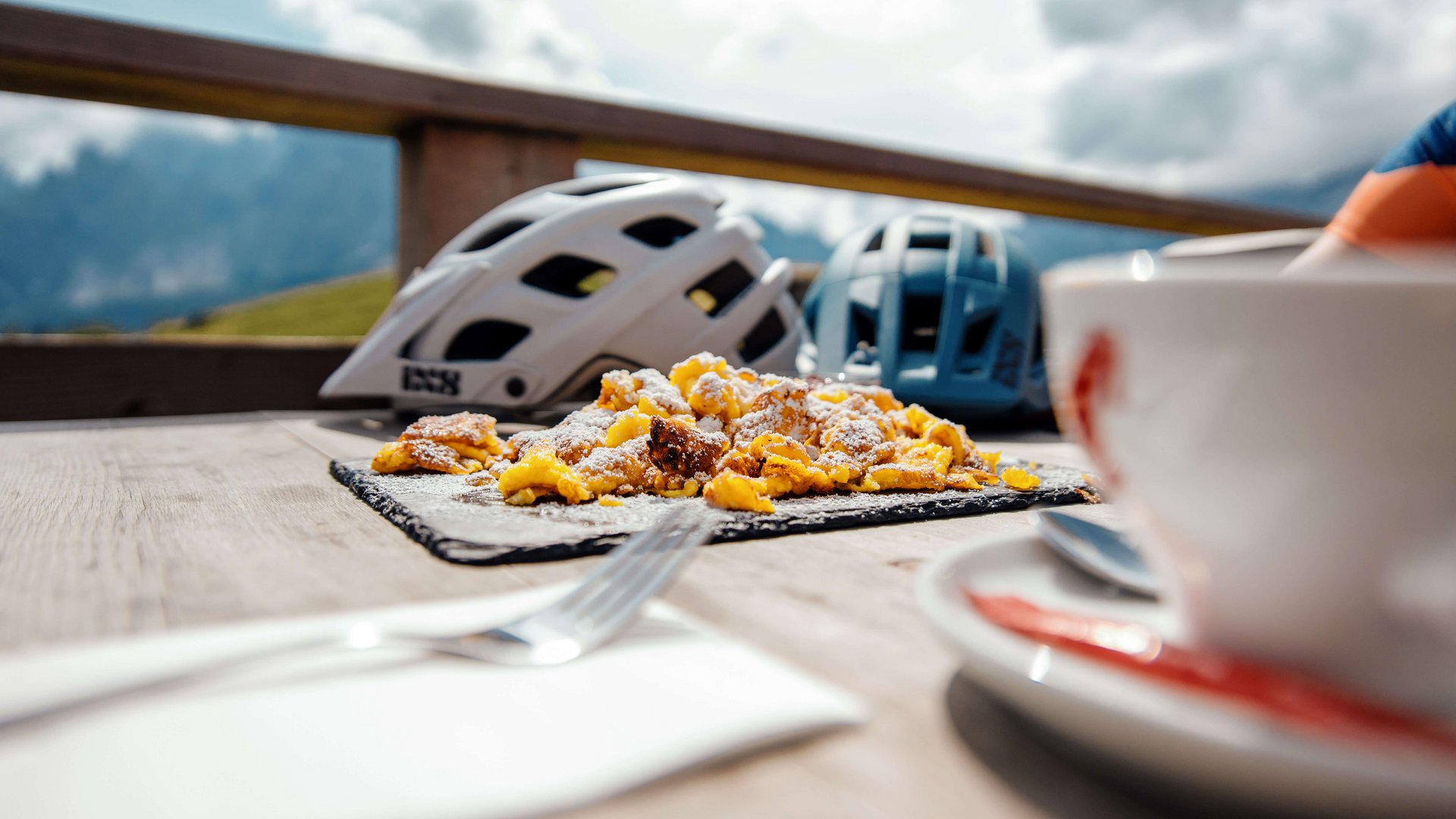 Bergfrühstück mit Kaiserschmarrn und Fahrradhelmen auf Holztisch