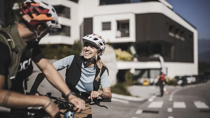 Frau und Mann mit Fahrradhelmen lachen draußen an einem sonnigen Tag