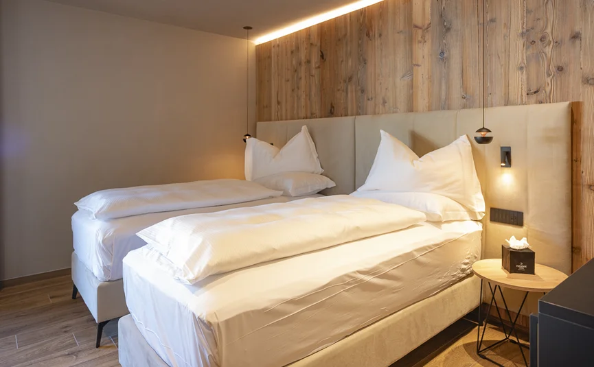 Zwei Einzelbetten mit weißen Bettwaren in einem modernen Zimmer mit Holzwand