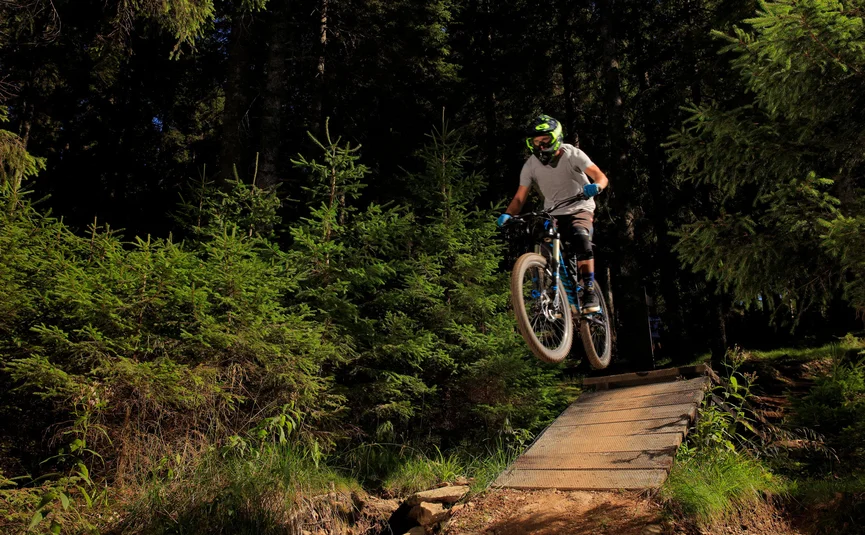 Mountainbiker springt op bospaadje in zonlicht