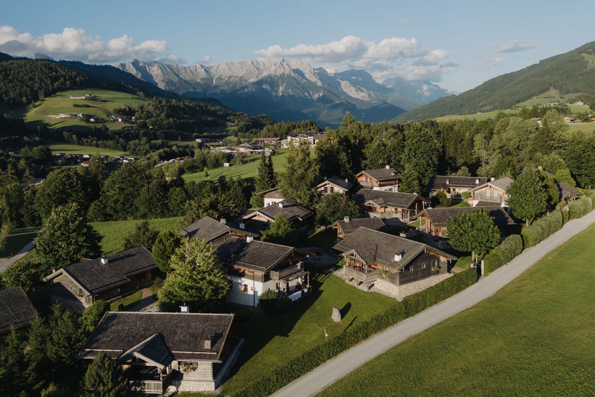 Dorf mit Holzhäusern und Bergen im Hintergrund bei sonnigem Wetter