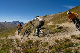 Drei Mountainbiker fahren einen kurvigen Bergpfad bei klarem Himmel hinunter