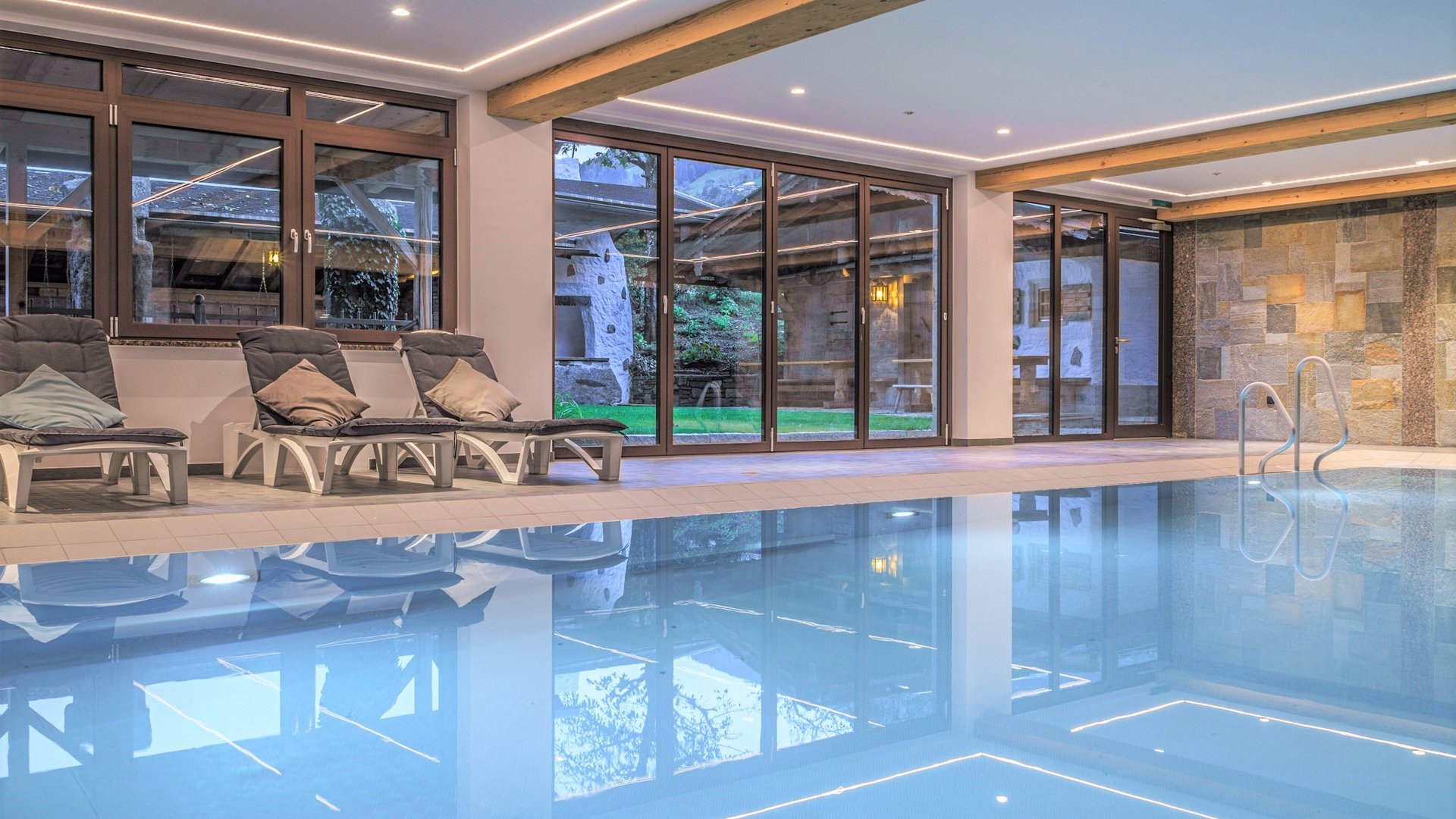Innenpool mit Liegestühlen und großen Fenstern zu einem Garten