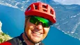 Mann mit rotem Fahrradhelm vor Berg und See in sonniger Landschaft