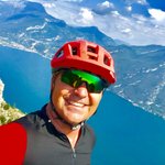 Mann mit rotem Fahrradhelm vor Berg und See in sonniger Landschaft