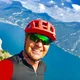 Mann mit rotem Fahrradhelm vor Berg und See in sonniger Landschaft