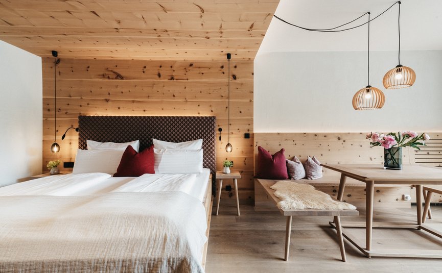 Biohotel Rupertus **** © Heldentheater Modern bedroom with wooden walls, table, bench, and red cushions