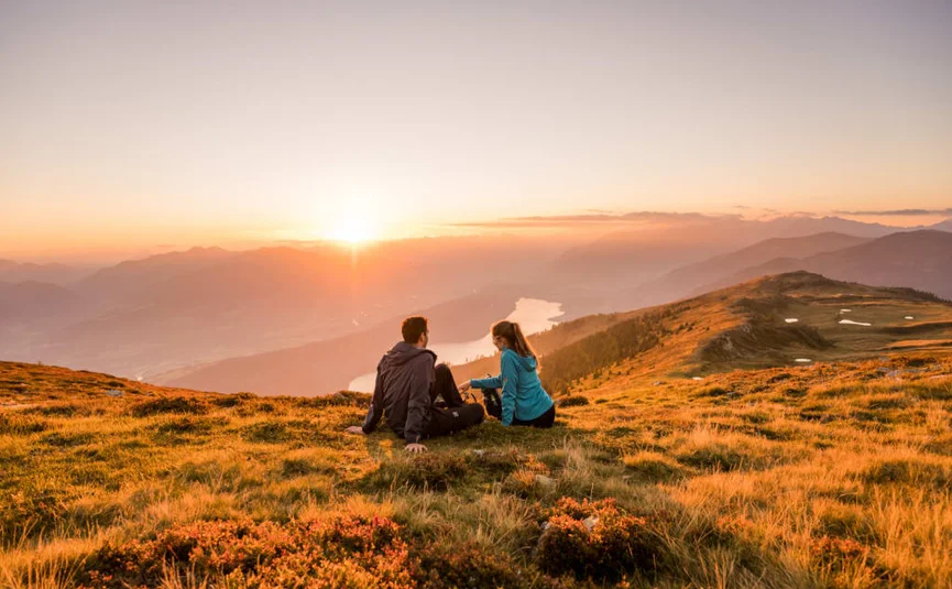 Koppel zit op heuvel en kijkt naar zonsondergang over bergen en meer