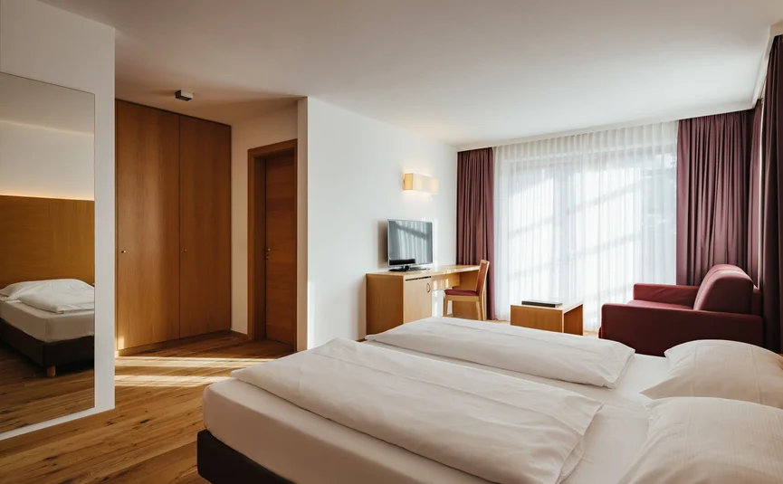 Helle, moderne Hotelzimmer mit Doppelbett, Arbeitsbereich und rotem Sessel