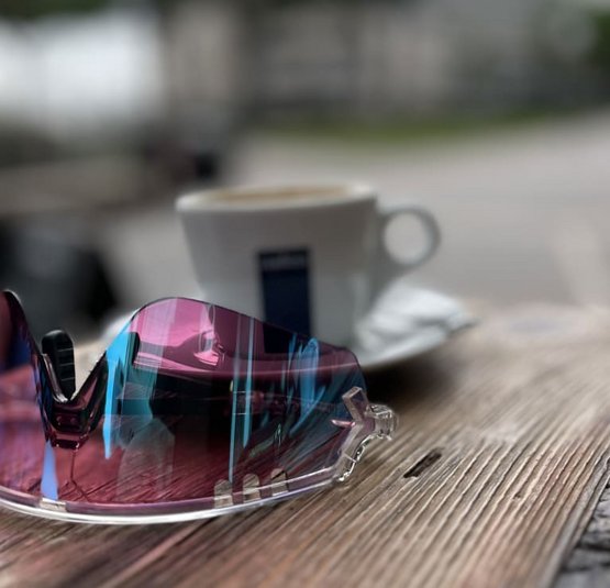 Bunte Sportbrille auf Holztisch mit unscharfer Kaffeetasse im Hintergrund