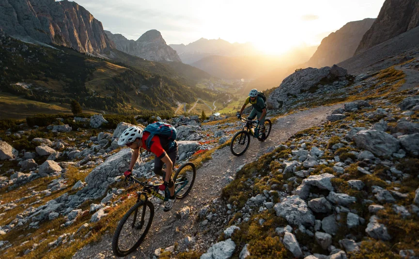 Two mountain bikers riding on rocky trail at sunset