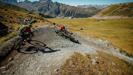 Zwei Mountainbiker fahren eine steile Kurve auf einem Bergtrail