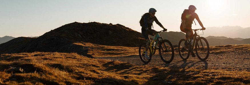 Zwei Mountainbiker fahren bei Sonnenuntergang auf einem Bergpfad
