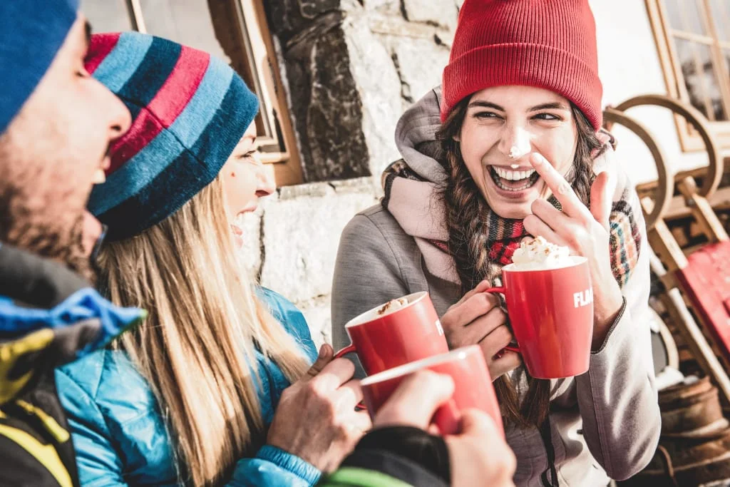 Freunde in Winterkleidung trinken heiße Getränke aus roten Tassen und lachen