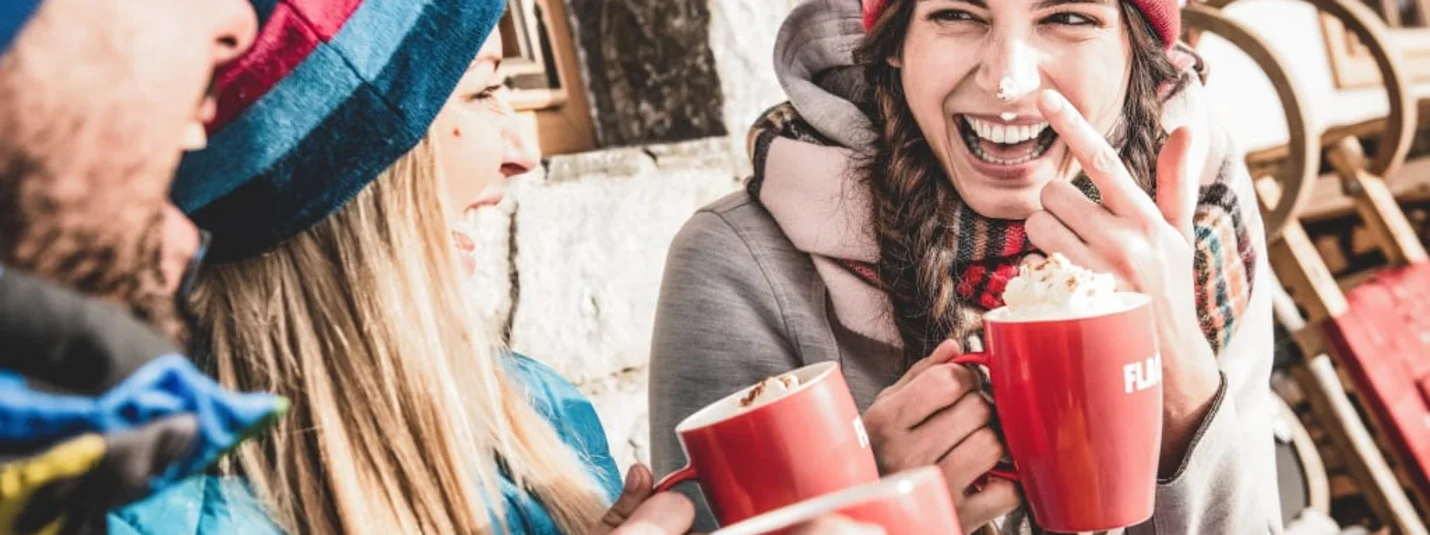 Freunde in Winterkleidung trinken heiße Getränke aus roten Tassen und lachen