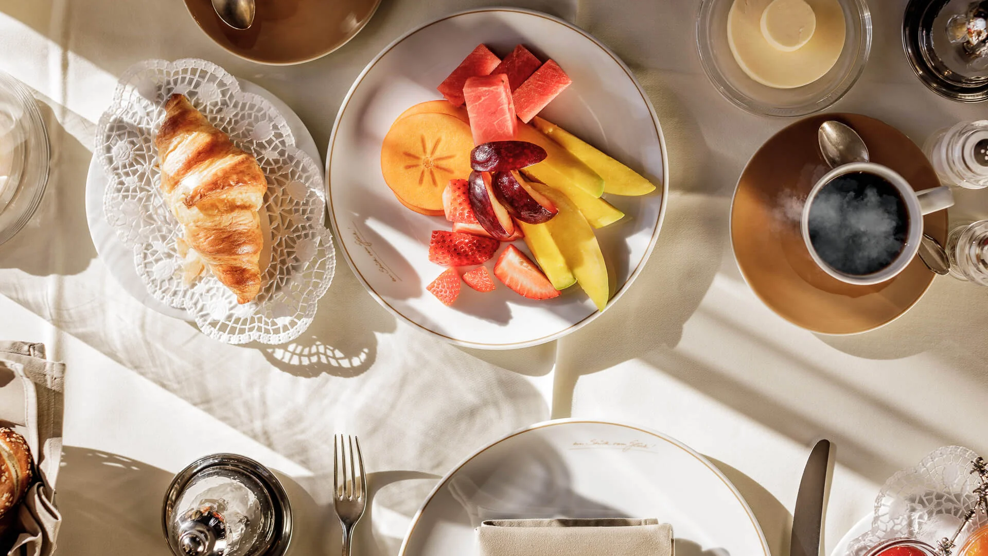 Frühstückstisch mit Croissant, Obstplatte und Kaffee