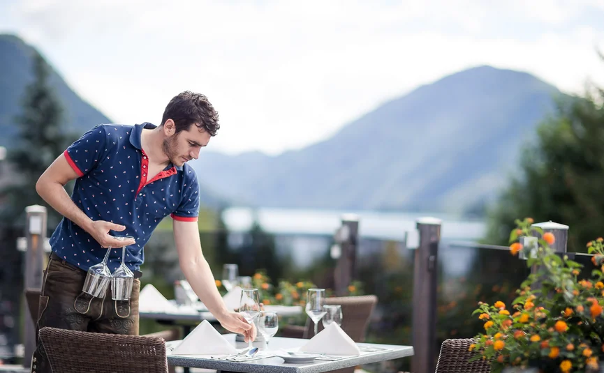 Kellner deckt Außentisch mit Weingläsern in Restaurant mit Bergblick