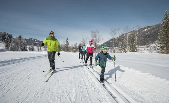 Familie beim Langlaufen auf einer schneebedeckten Loipe im Winter