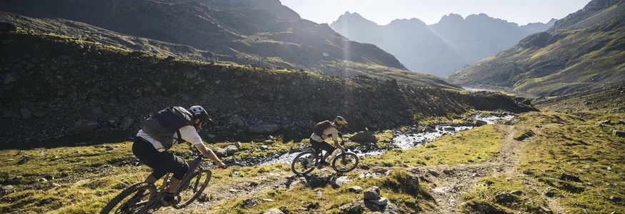 Zwei Mountainbiker fahren auf einem bergigen Pfad im Sonnenschein