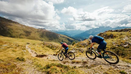 Zwei Mountainbiker fahren auf einem bergigen Pfad bei bewölktem Himmel
