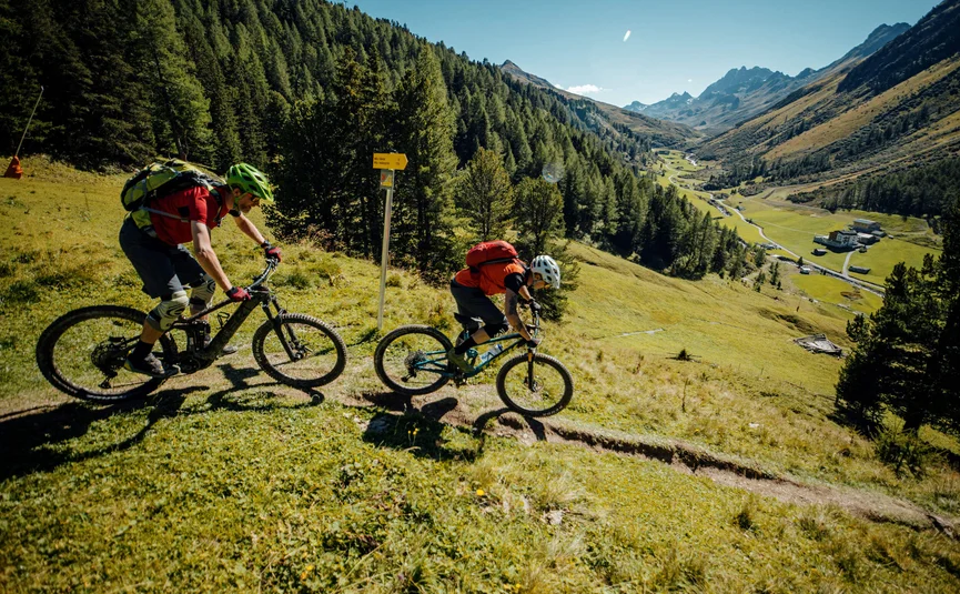 Zwei Mountainbiker fahren auf einem Bergweg mit Blick auf ein Tal