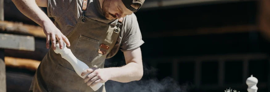 Mann würzt Essen über einem Grill mit einer Gewürzmühle