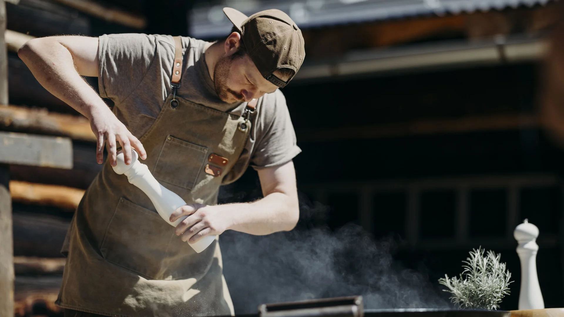 Mann würzt Essen über einem Grill mit einer Gewürzmühle