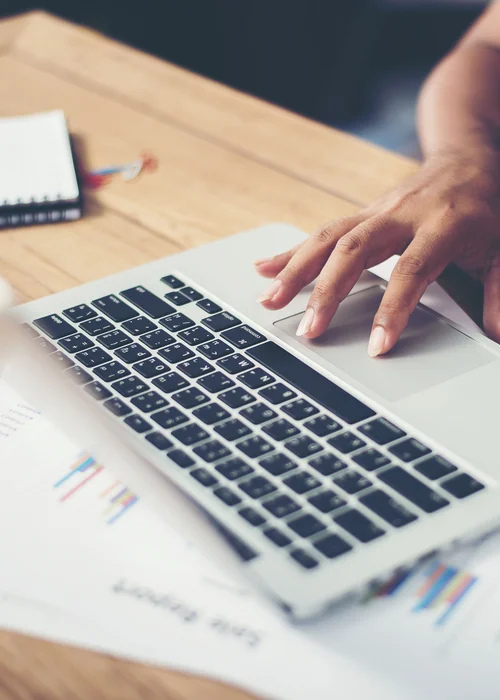 Hand bedient Laptop-Touchpad auf Holztisch mit Unterlagen