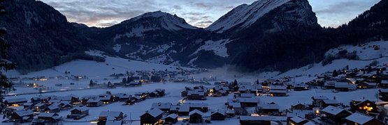 Snow-covered houses in a valley with mountains at dusk