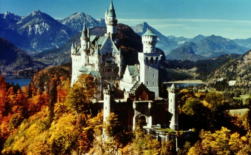 Schloss Neuschwanstein umgeben von Herbstlaub und Bergen im Hintergrund