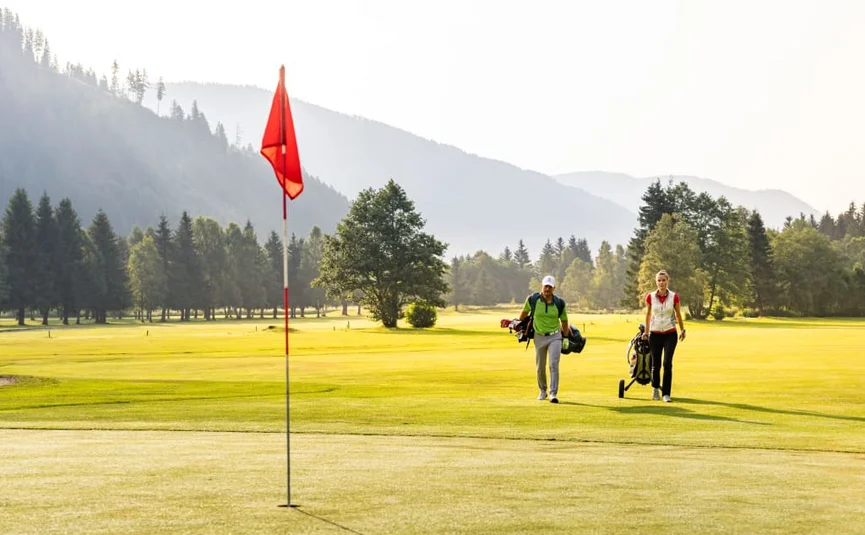 Two golfers walking with golf bags on green golf course with mountains