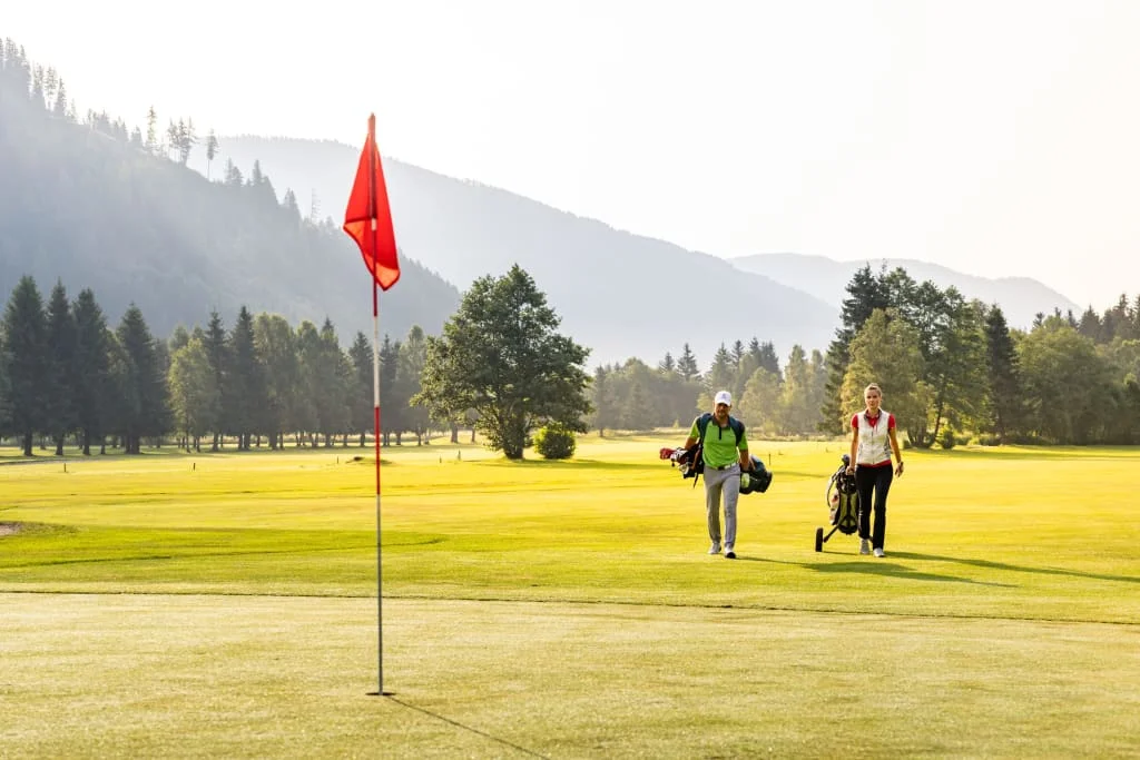 Zwei Golfer mit Golftaschen auf grünem Golfplatz bei Bergkulisse
